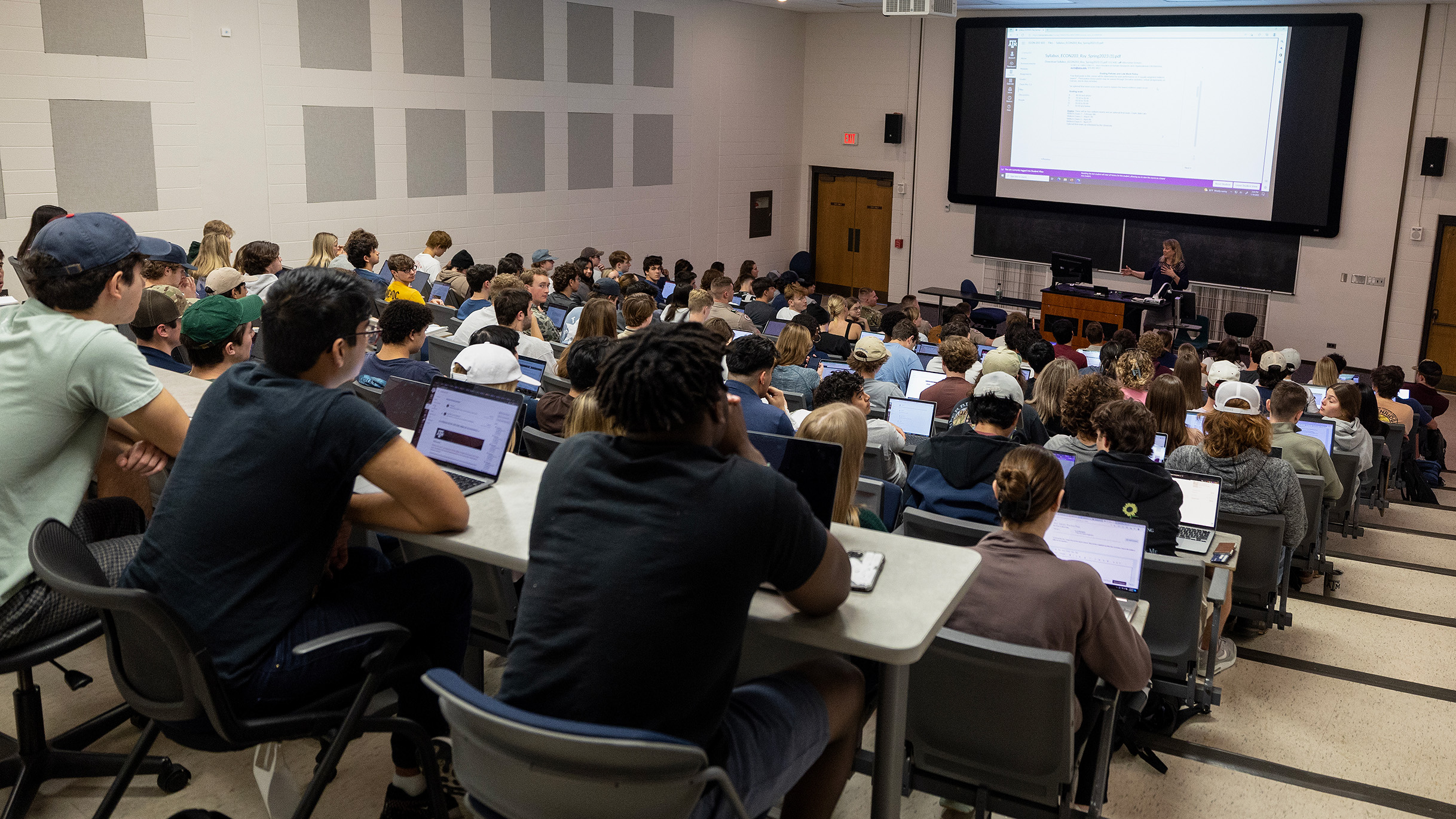 A lecture hall full of people looking at a large presentation screen.