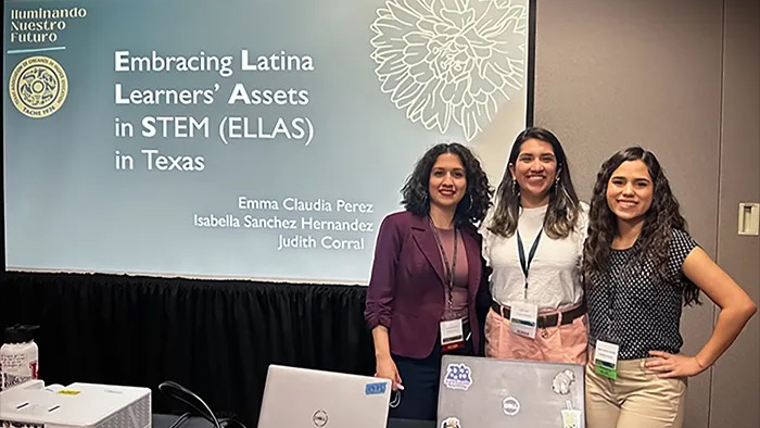 Three women and a conference standing in front of a presentation screen.